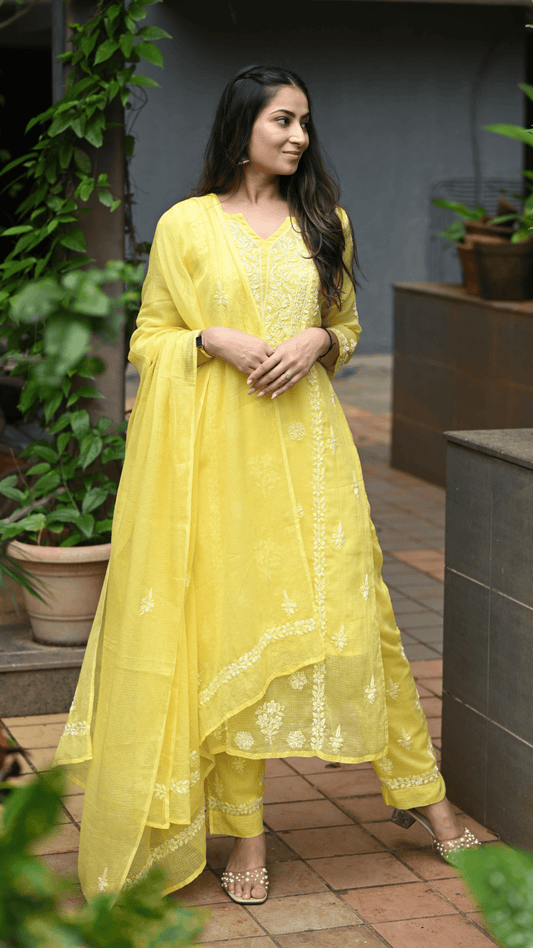 Woman wearing a yellow traditional outfit with a floral pattern in an outdoor setting.