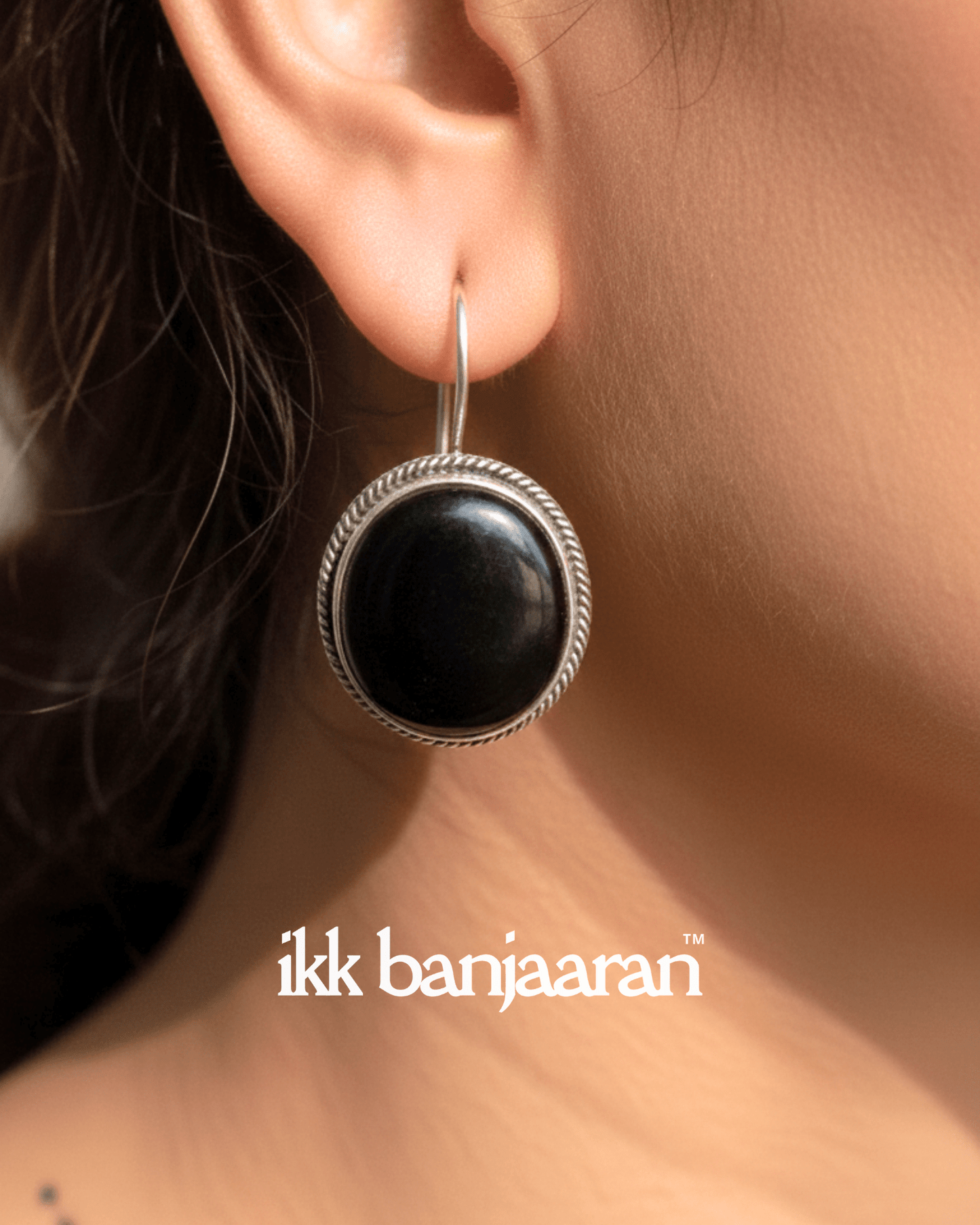 Black earring on an ear with 'ikk banjaaran' branding.