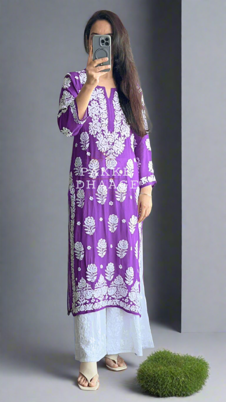 Person wearing a purple and white patterned dress taking a mirror selfie in a room with plants.