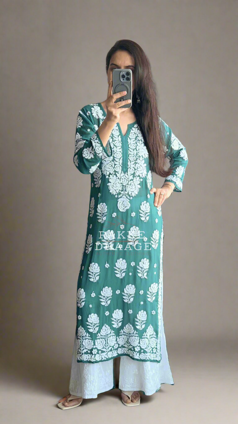 Person wearing a green and white floral chikankari suit standing in front of a mirror with plants around.