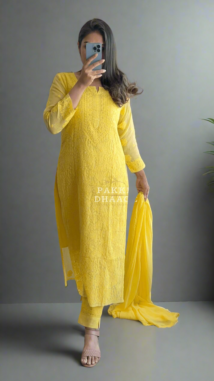 Person wearing a yellow chikankari outfit standing in front of a mirror with plants around.