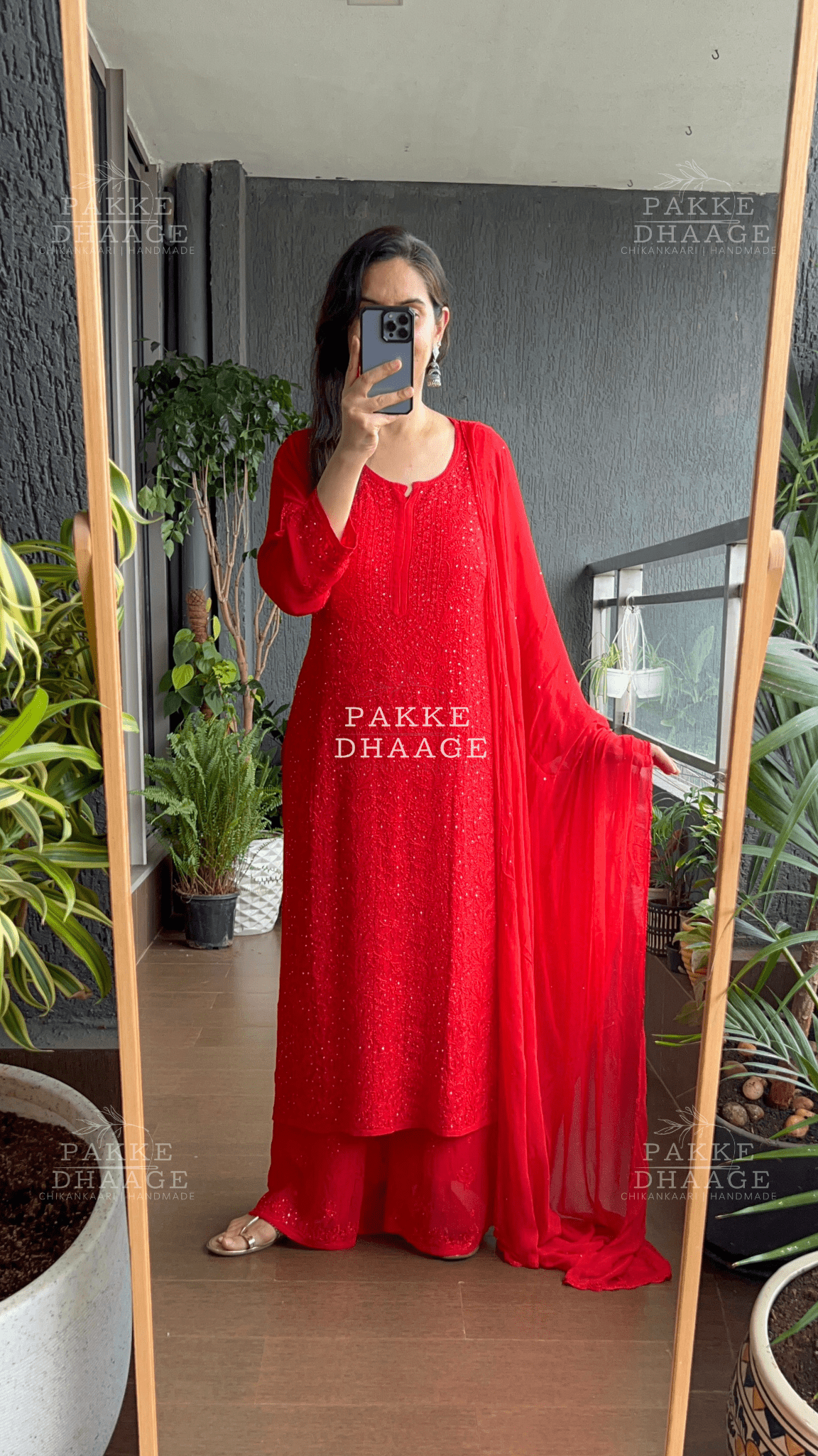 Woman wearing a dright red chikankari dressin a room with plants.
