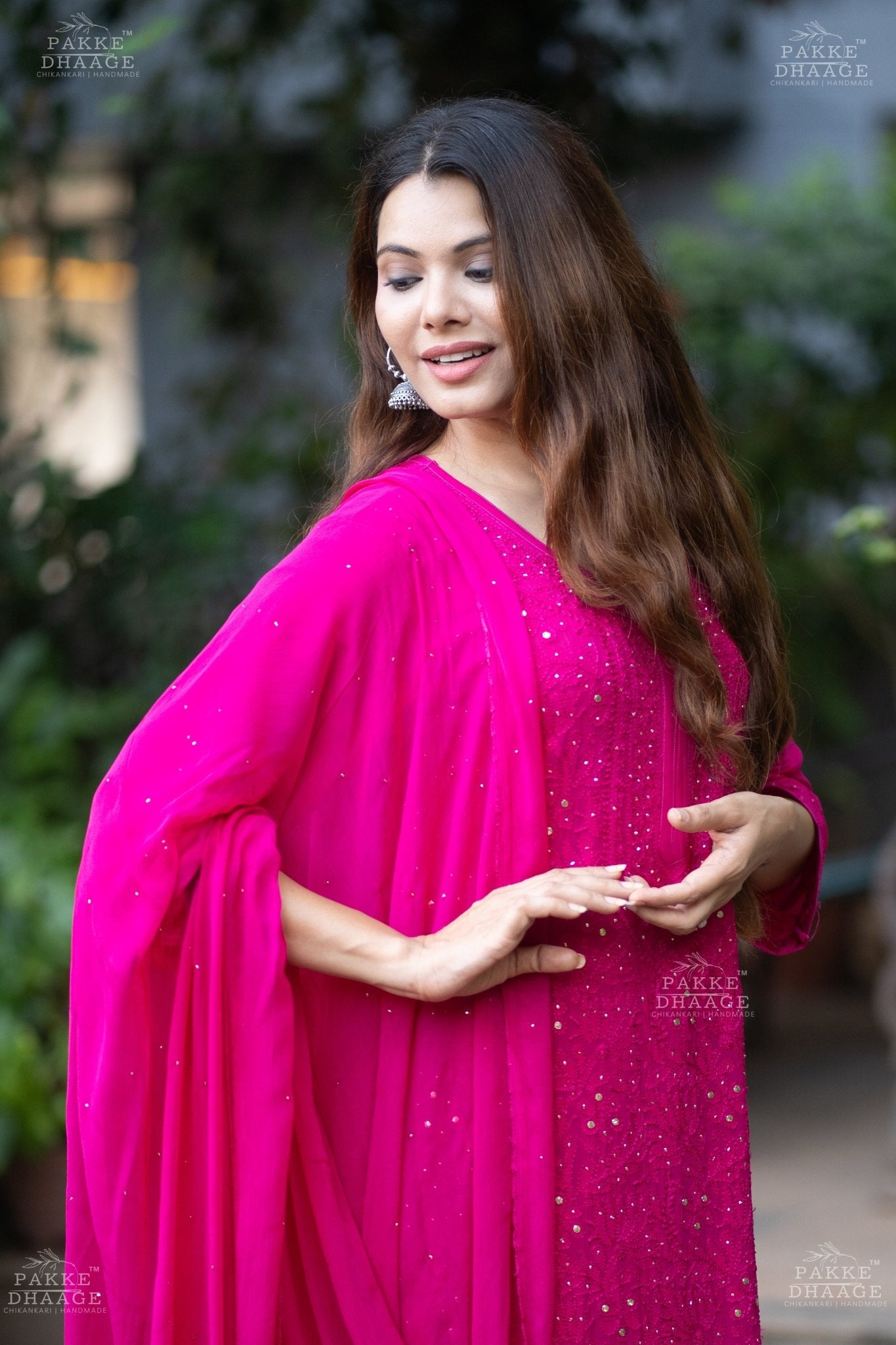Woman wearing a bright pink chikankari suit set with delicate mukaish work, with a blurred background