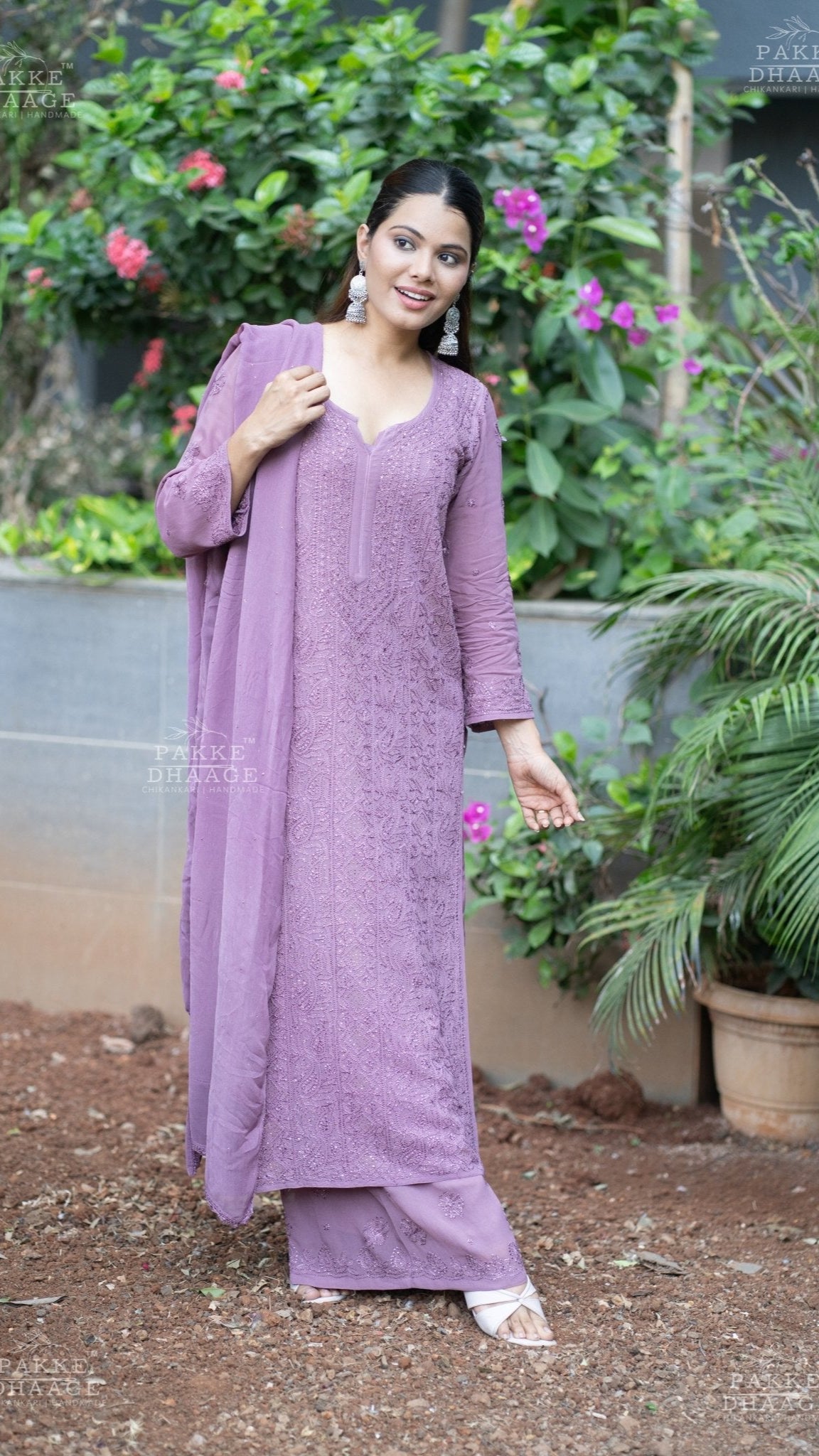 Woman in a plum chikankari hand embroidered outfit standing outdoors with greenery in the background