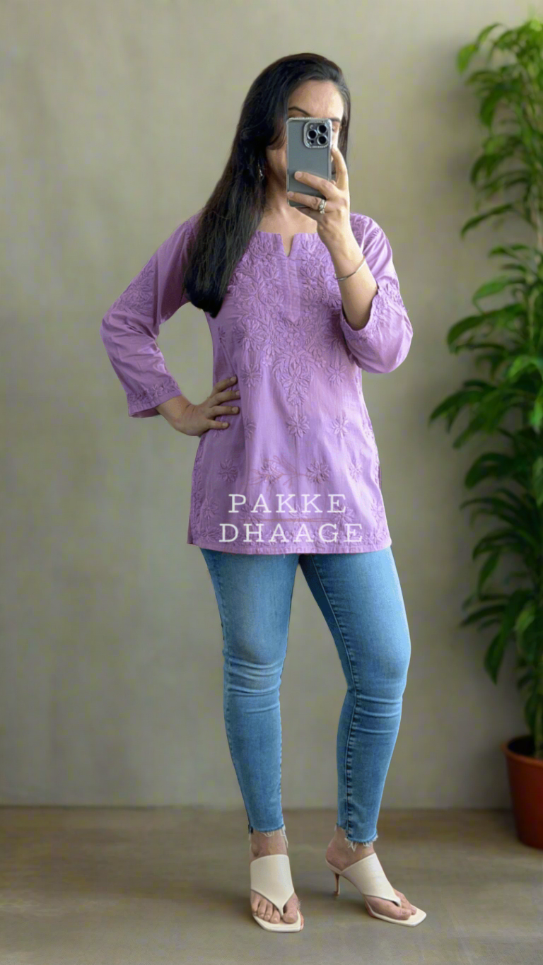 Person wearing a purple short top with chikankari and blue jeans standing in front of a mirror with plants around.