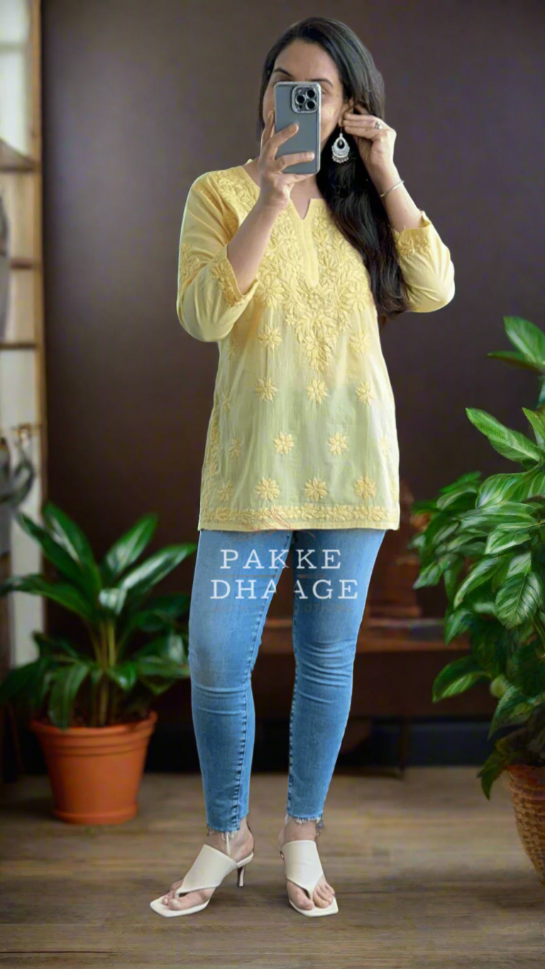 Woman wearing a chikankari yellow top and blue jeans, surrounded by plants.