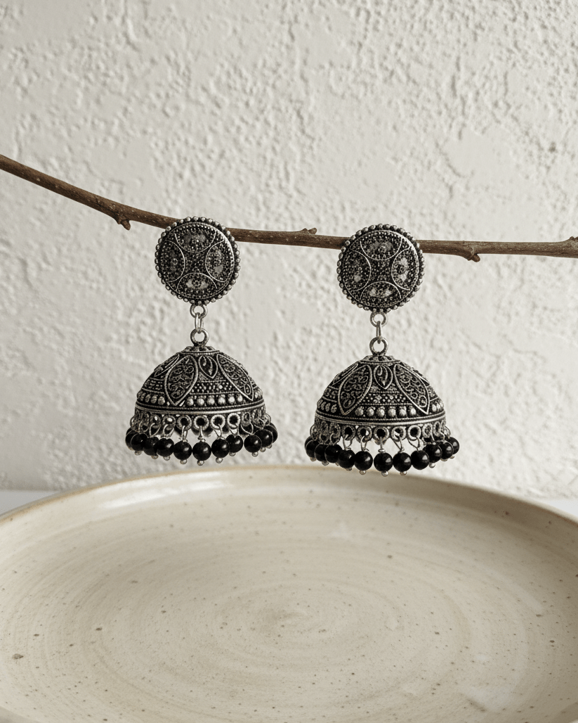 Pair of silver and black earrings on a branch against a white background