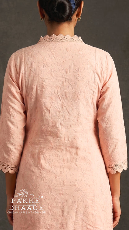 A woman viewed from the back wearing a light peach-pink textured kurta with lace trim at the collar and cuffs. The brand name 'PAKE DHAAGE' is visible as a watermark at the bottom left.