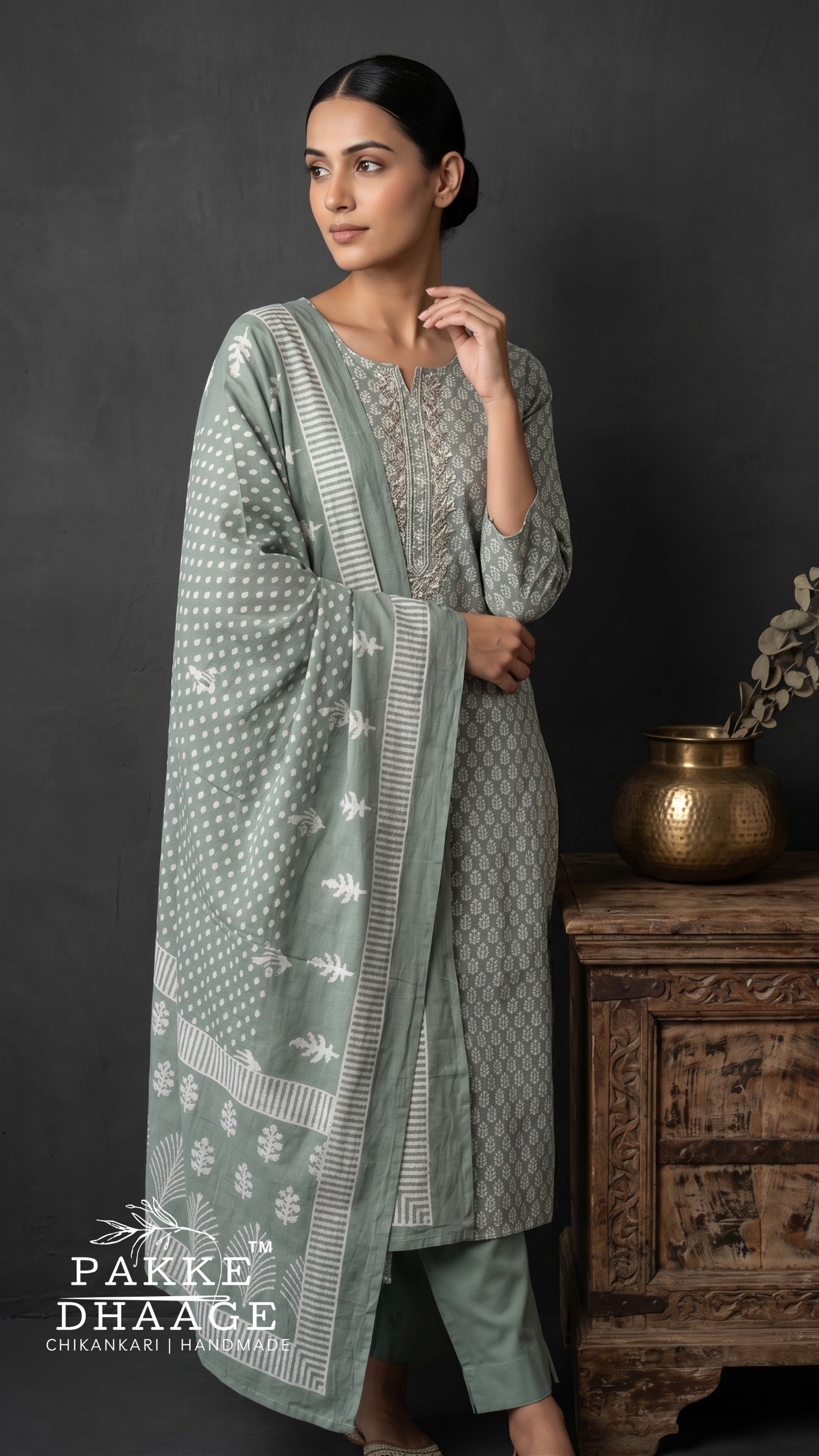 A woman models a three-piece traditional outfit in sage green and gray with white block prints. The set includes a long kurta, matching trousers, and a draped dupatta. | Pakke Dhaage