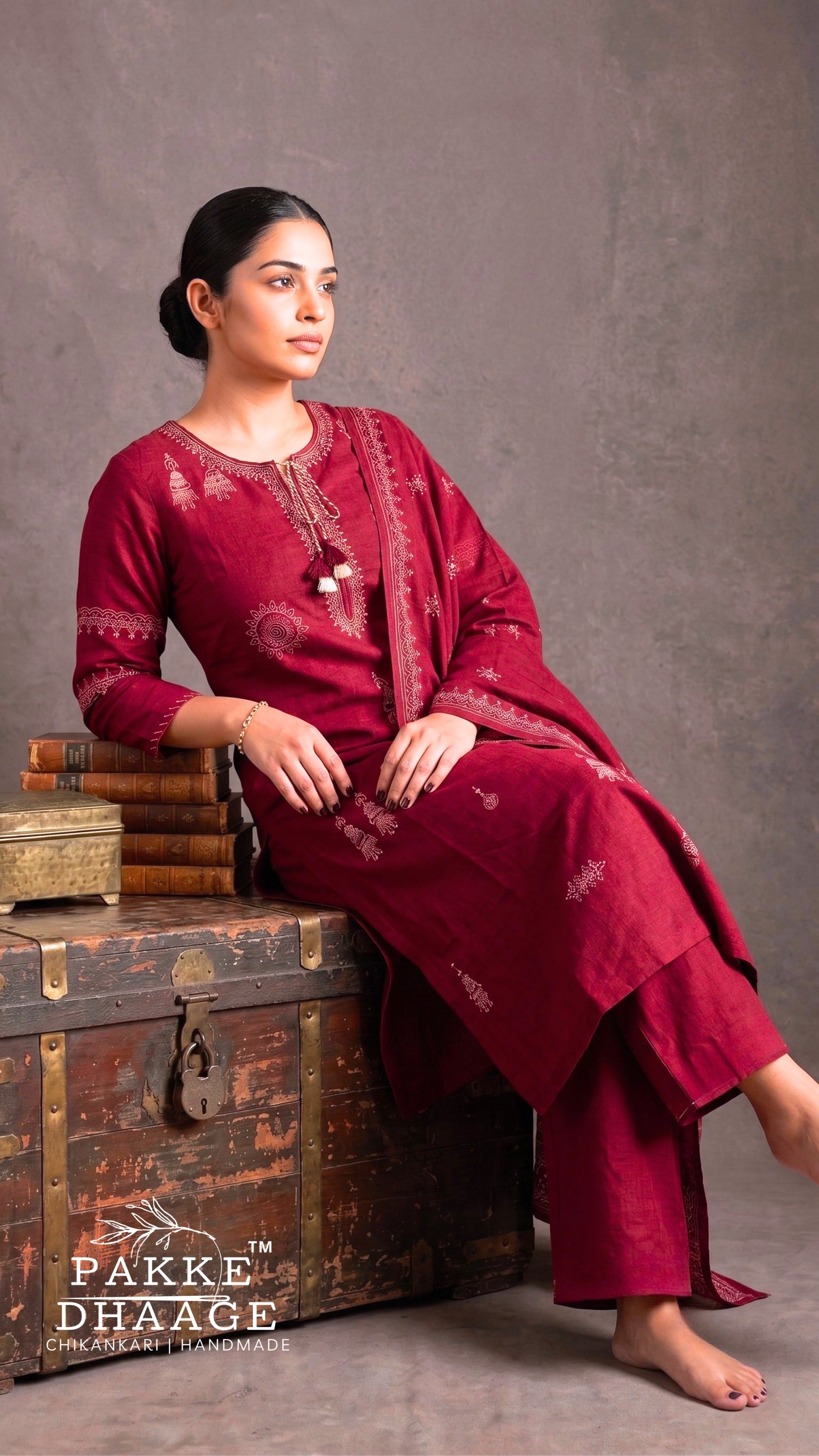 Model wearing a deep maroon pure cotton straight kurta set featuring fine cream floral thread embroidery on the V-neckline with tassels and matching dupatta. | PAKKE DHAAGE