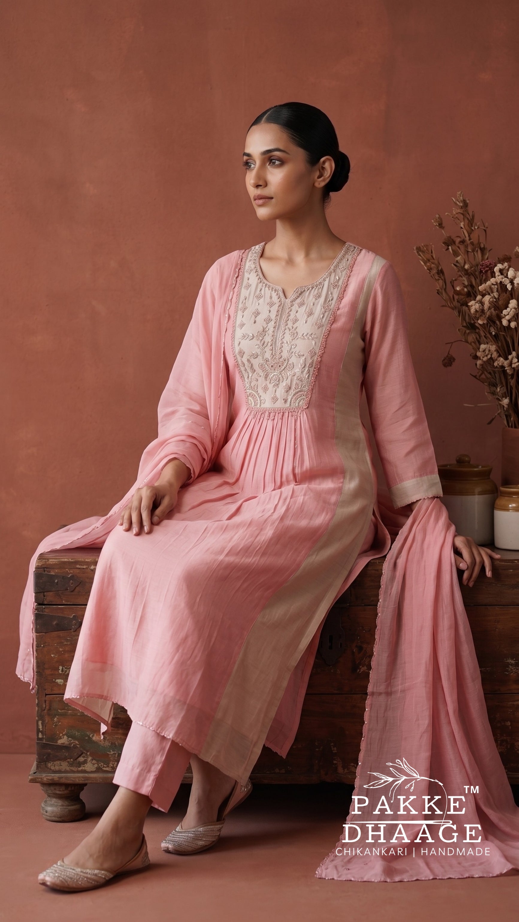 Model sitting wearing a beige and blush pink Mul Chanderi straight kurta set featuring fine embroidery on the pink yoke, pin-tuck pleats, and a draped sheer dupatta. | Pakke Dhaage