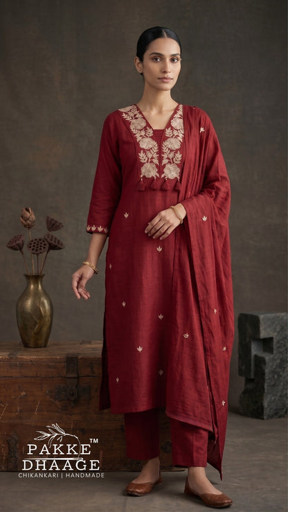 A woman models a deep maroon red ethnic salwar kameez suit by Pakke Dhaage, featuring beige floral embroidery on the chest and scattered gold zari motifs, paired with matching trousers and a dupatta.