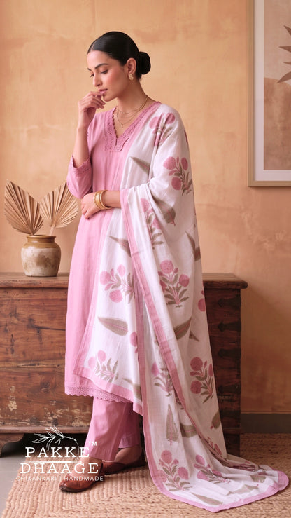 A woman models a traditional South Asian outfit consisting of a light pink kurta and matching trousers, paired with a white dupatta featuring pink floral patterns, in a warm-toned indoor setting. | Pakke Dhaage
