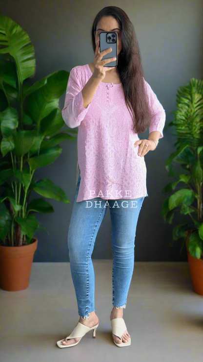 Person taking a mirror selfie wearing a chikankari pink top and blue jeans on a balcony with plants.