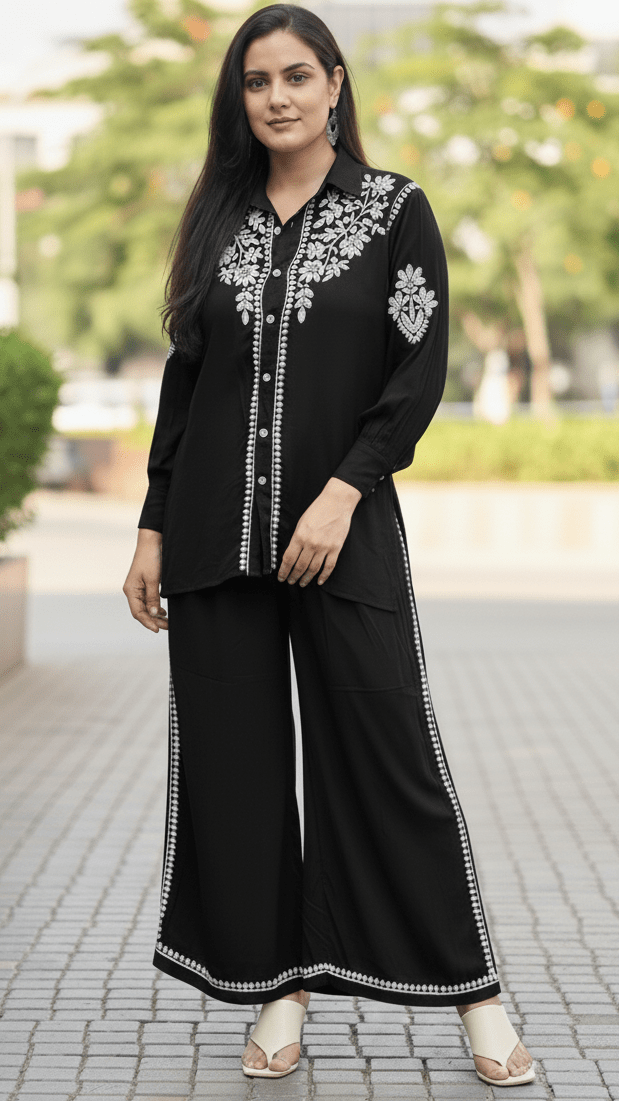 Woman wearing a black outfit with white embroidery standing outdoors.