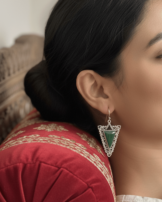 Woman wearing a silver earring with a green gemstone, sitting on a decorative cushion.