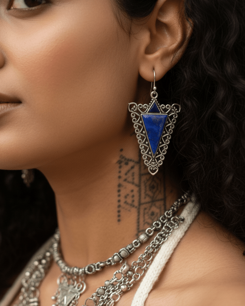 Close-up of a woman wearing silver and blue triangular earrings with intricate designs.