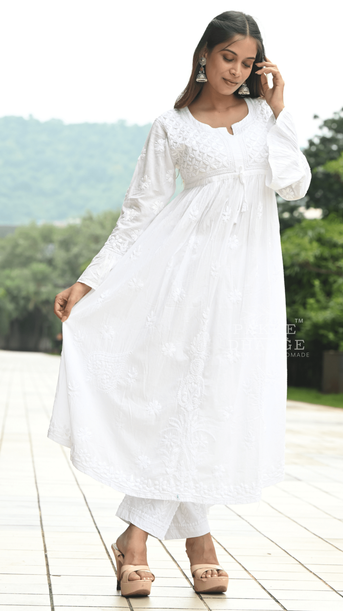 Woman in a white chikankari outfit standing on a wooden deck with greenery in the background