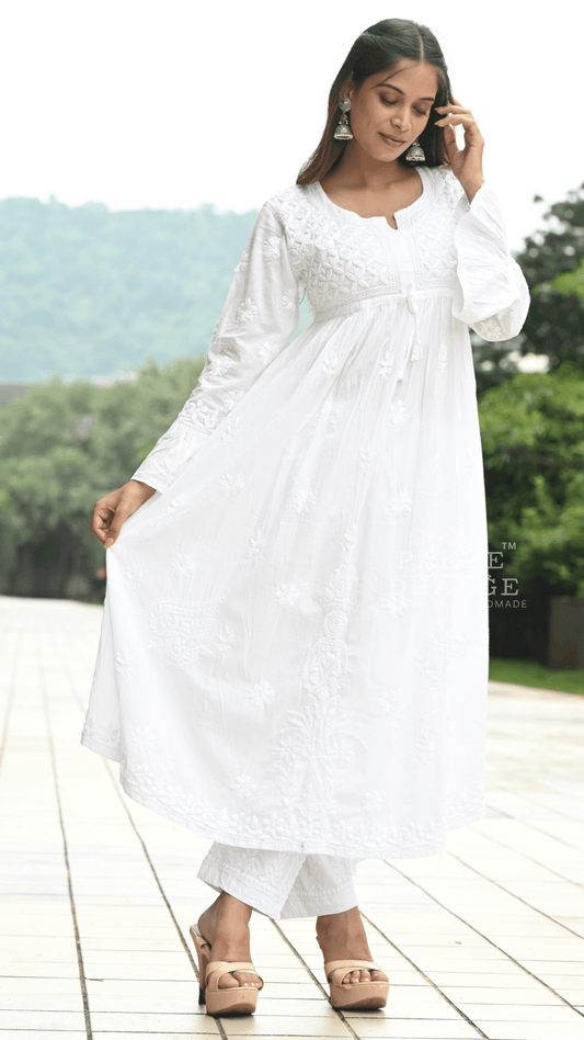 Woman in a white chikankari outfit standing on a wooden deck with greenery in the background