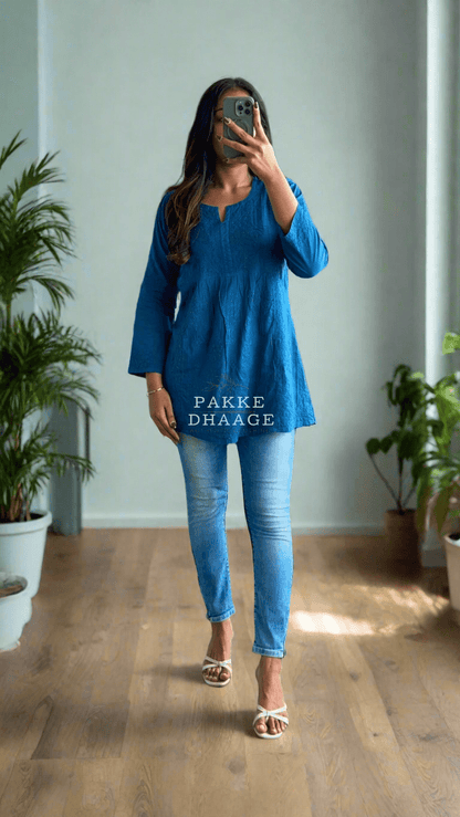 Person in a blue outfit standing in a room with plants.