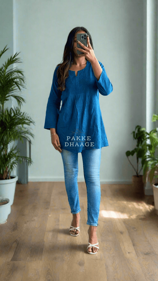 Person in a blue outfit standing in a room with plants.