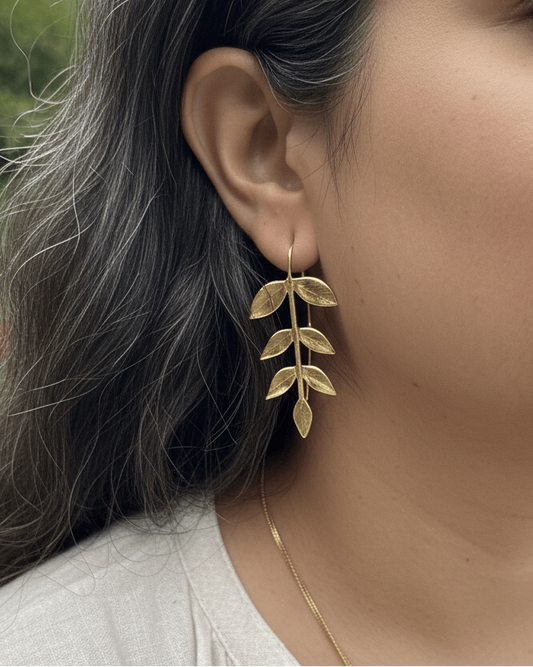 Close-up of a person wearing gold leaf earrings with a blurred background
