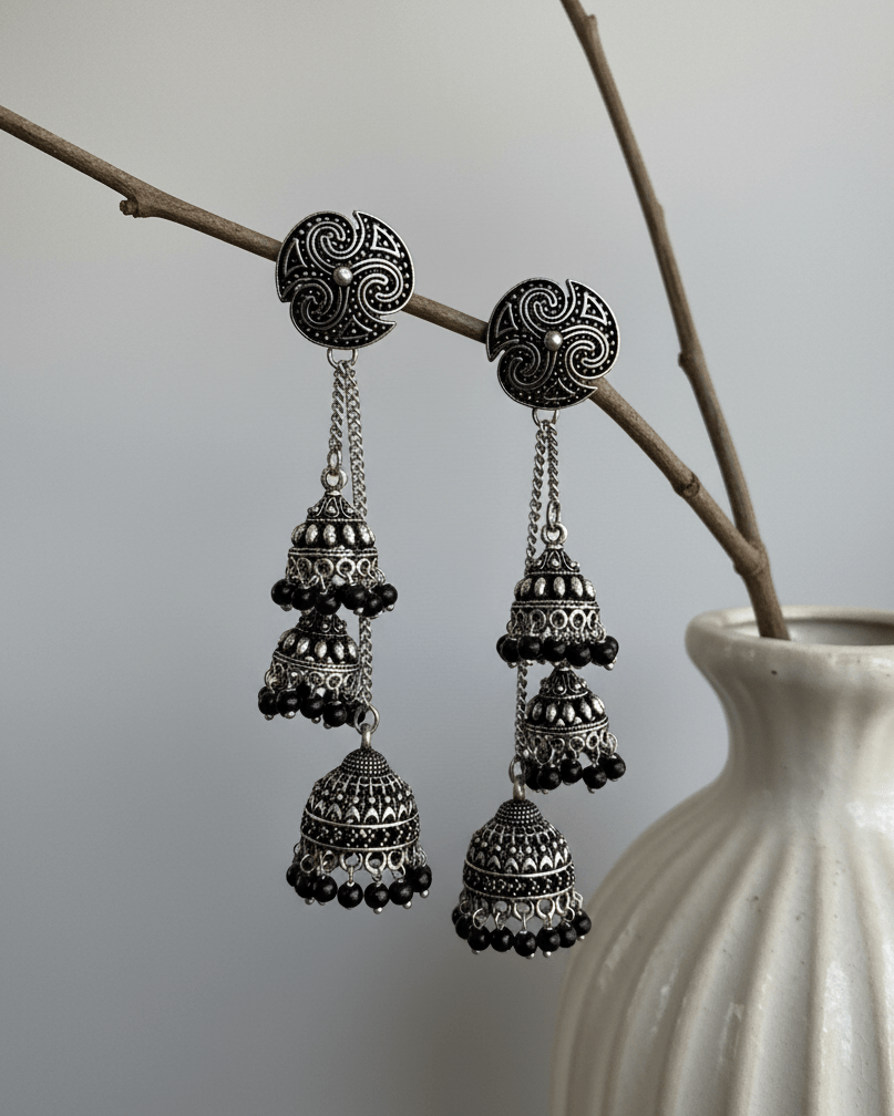 Ornate oxidised silver cascade earrings hanging from a branch with a vase in the background