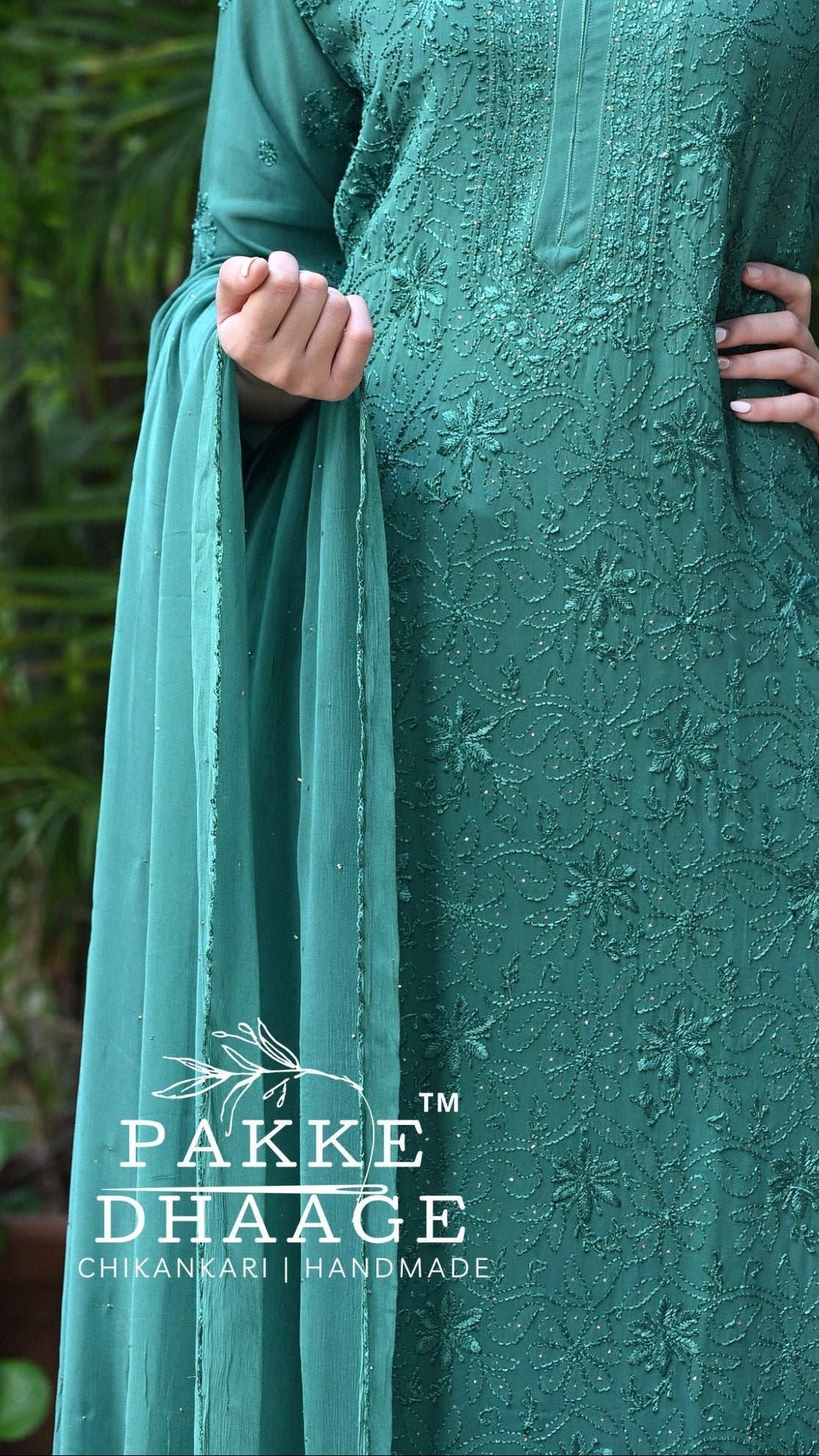 Woman wearing a bottle green embroidered outfit with 'Pakke Dhaage' branding in an outdoor setting.