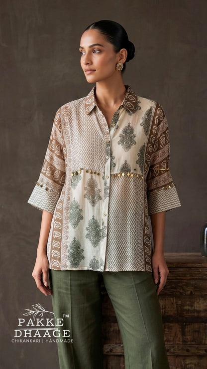 A woman modeling a beige and brown printed kurta with green leaf motifs and gold embroidery, paired with olive green trousers, set against a rustic brown background. The brand logo 'PAKKE DHAAGE' is visible in the bottom left corner.