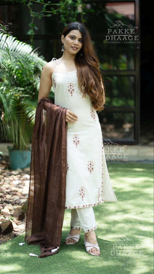 Woman in a white printed suit set  with a brown dupatta standing outdoors.