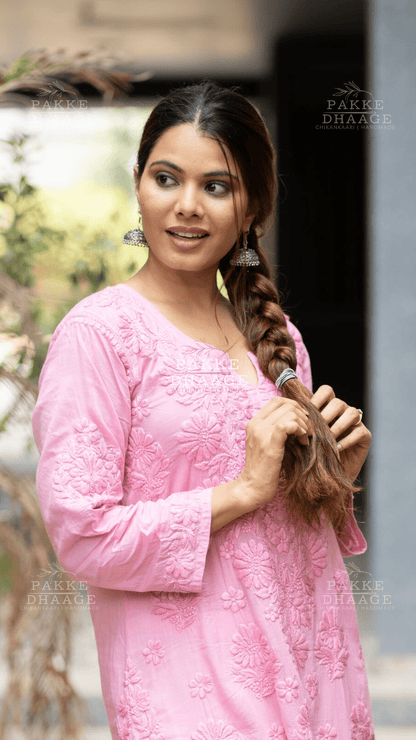 Woman in a pink traditional handmade chikankari kurti with braided hair, standing outdoors.