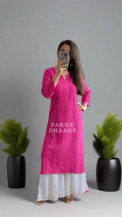 Person wearing a bright pink kurta with white pants standing in front of a mirror.