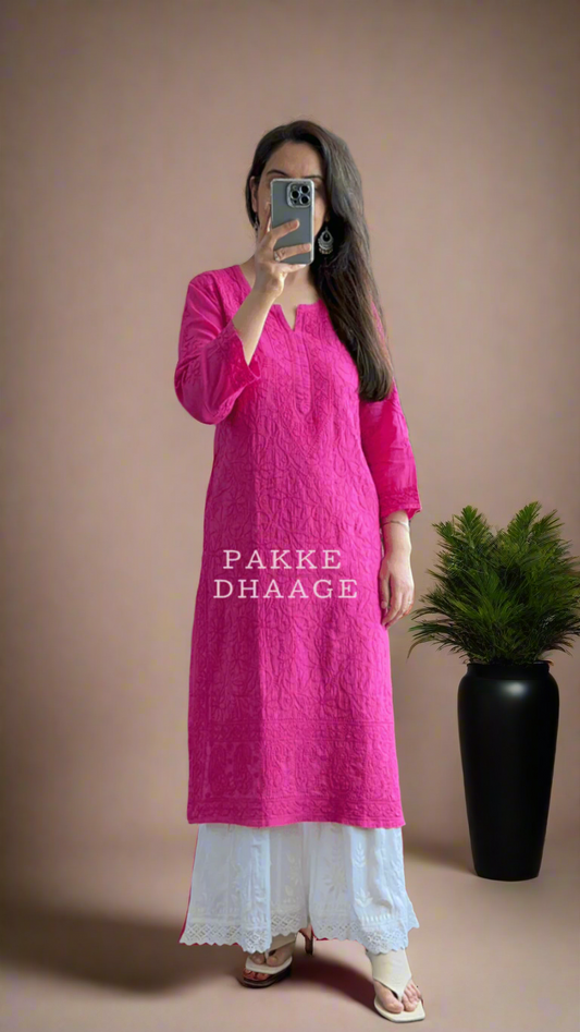 Person wearing a bright pink kurta with white pants standing in front of a mirror.