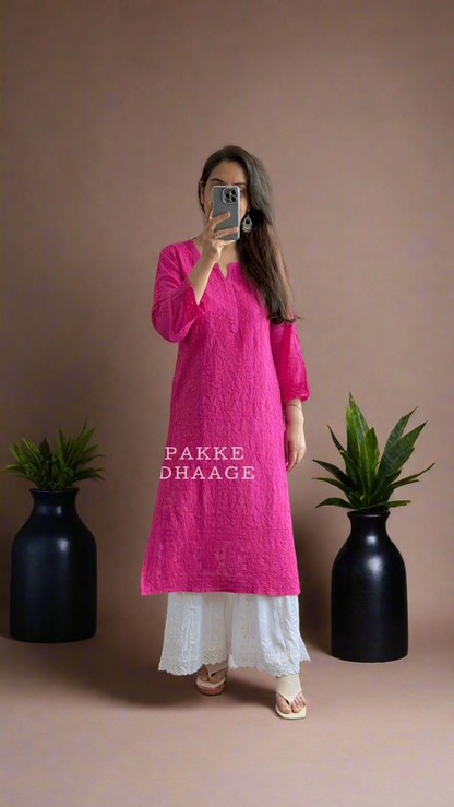 Person wearing a bright pink kurta with white pants standing in front of a mirror.