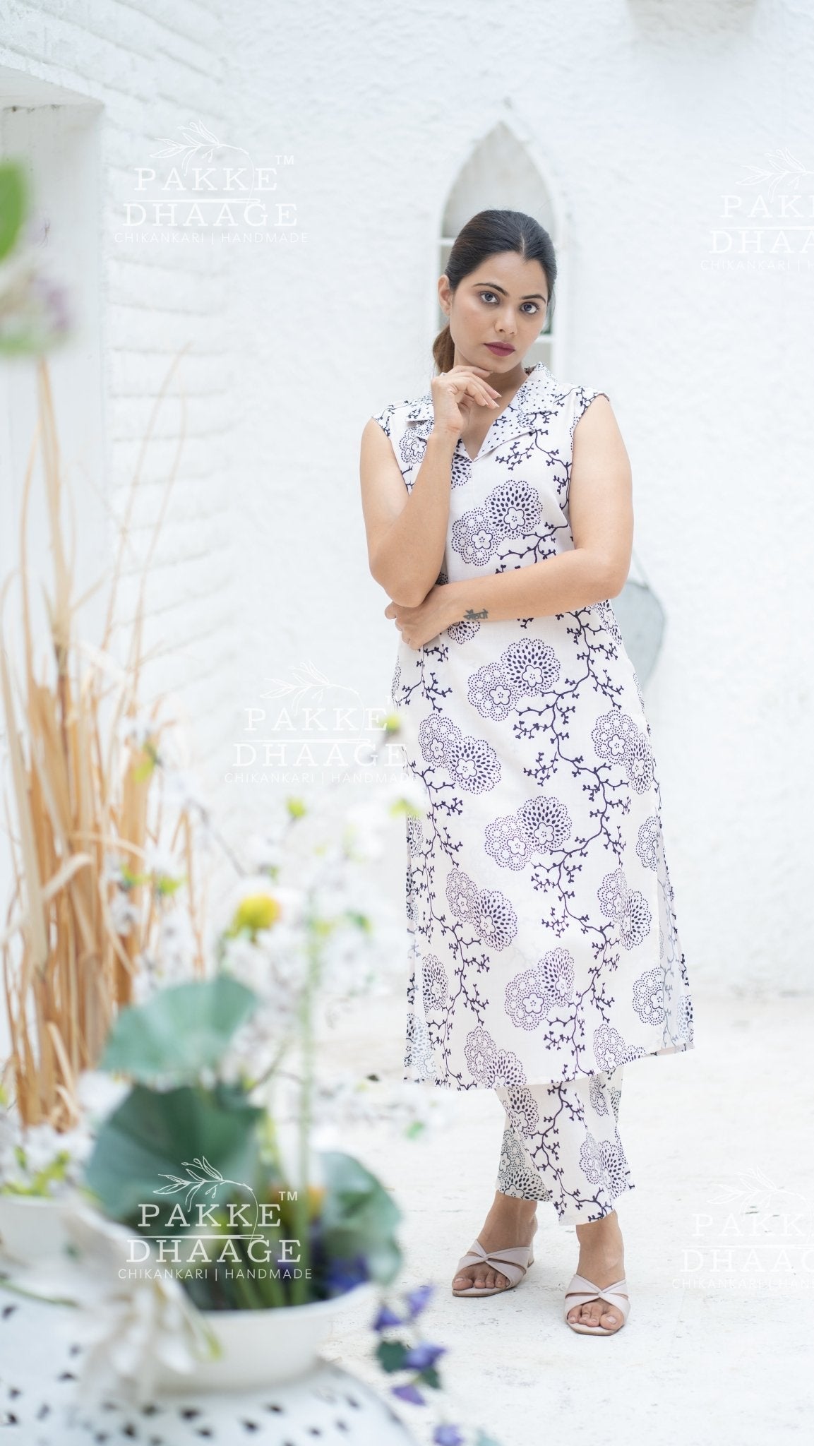 Woman wearing a floral suit set, with purple printed floral pattern in a decorated indoor setting with plants.