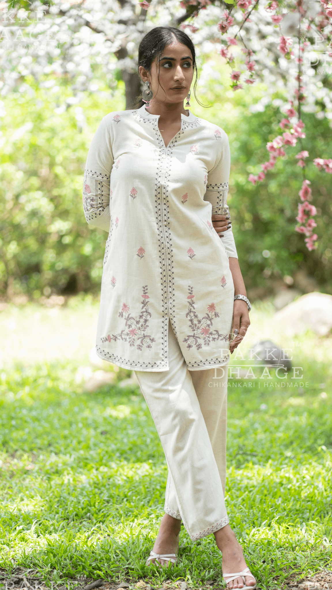 Woman in a white printed co-ord set with minimalistic prints standing in a garden with greenery and flowers.