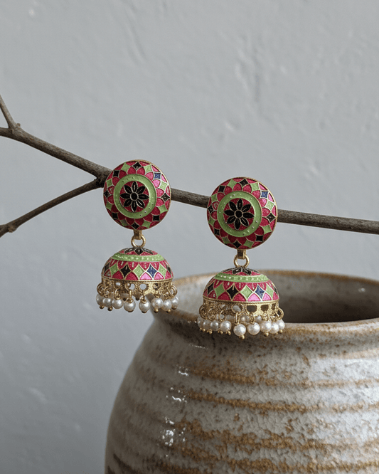 Decorative meenakari handmade earrings with intricate designs on a branch over a textured pot.