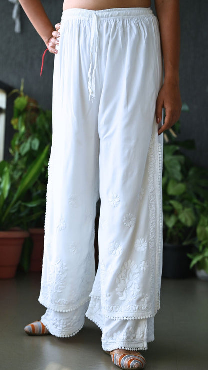 White wide-leg embroidered pants with a drawstring waist, shown on a model in an indoor setting with potted plants in the background. | Pakke Dhaage