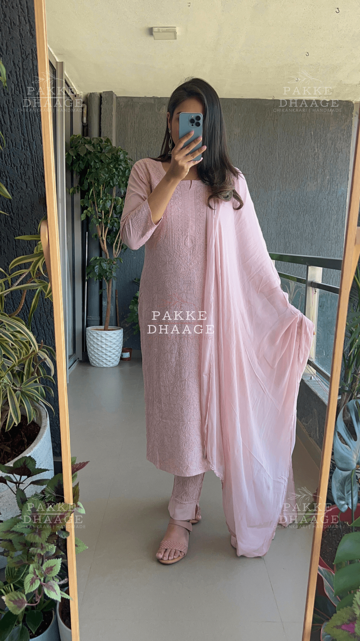 Person wearing a pink traditional chikankari outfit with 'PAKKE DHAAGE' branding in a room with plants.