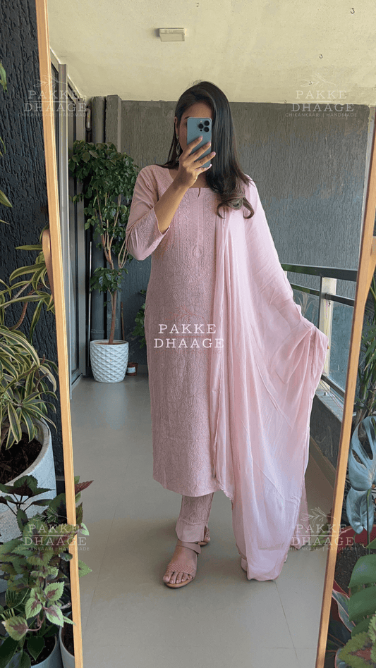 Person wearing a pink traditional chikankari outfit with 'PAKKE DHAAGE' branding in a room with plants.