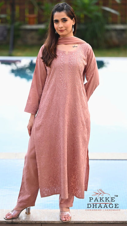 A woman wearing a dusty rose pink embroidered kurta set with matching trousers and a dupatta, standing by a swimming pool. The brand logo 'PAKE DHAAGE' is visible in the bottom right corner.