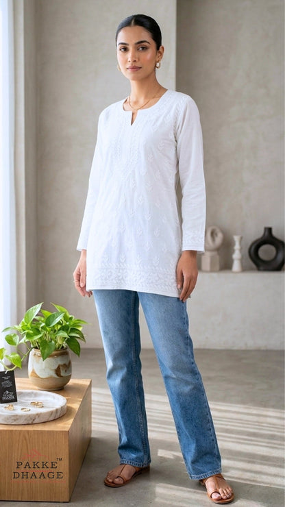 Woman wearing a white chikankari top and blue jeans standing in a room with decor elements.