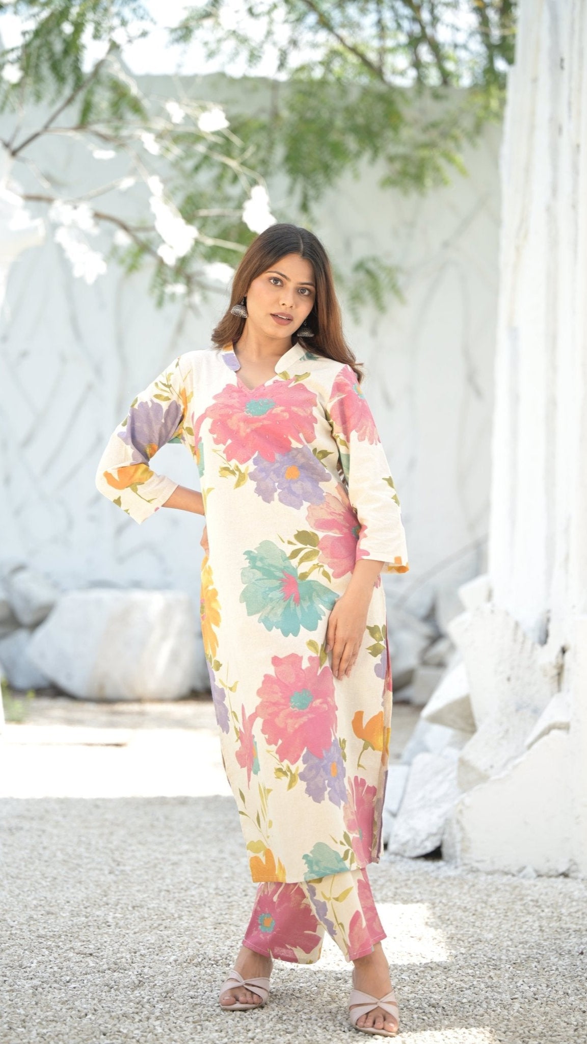 Woman wearing a floral printed kurti set standing outdoors with white decorative elements in the background