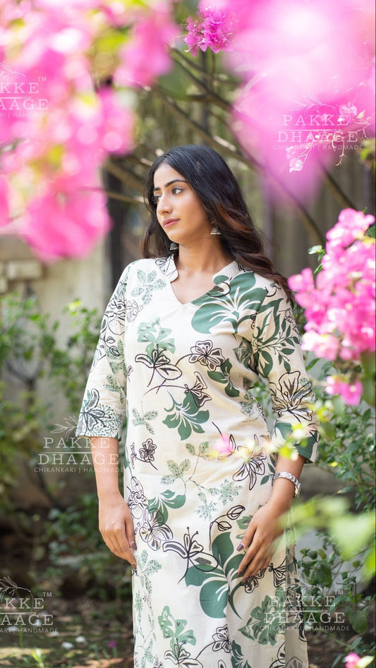 Woman in a floral kurti set standing among pink flowers with 'Pakke Dhaage' branding.
