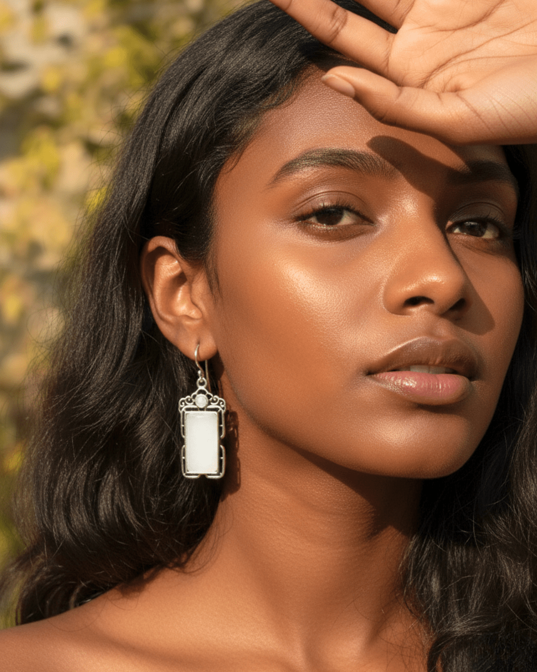 Woman wearing a silver earring with a rectangular pendant against a blurred natural background