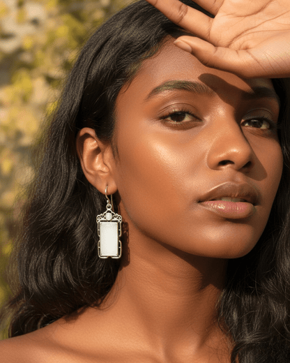 Woman wearing a silver earring with a rectangular pendant against a blurred natural background