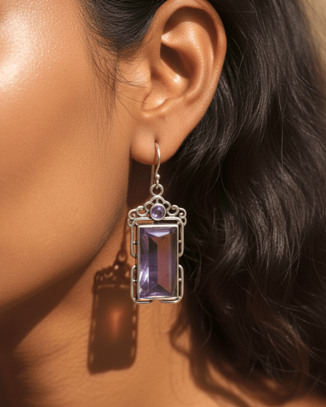 Close-up of an earring with a purple gemstone worn by a person.