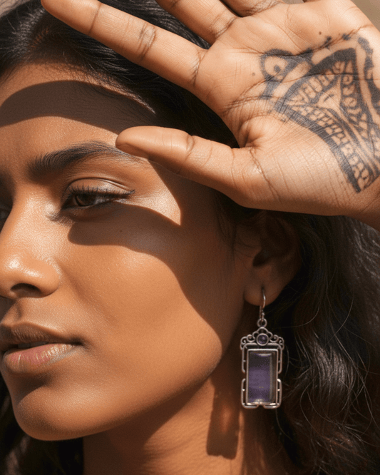 Close-up of a woman's face with a hand touching her forehead, wearing a purple handmade oxidized earring.