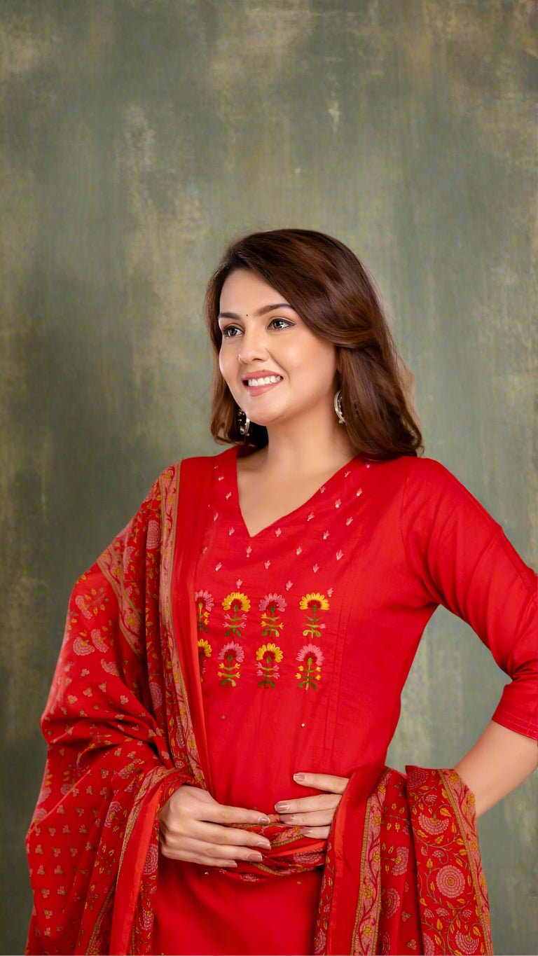Woman wearing a red traditional kurti set with dupatta against a textured wall.