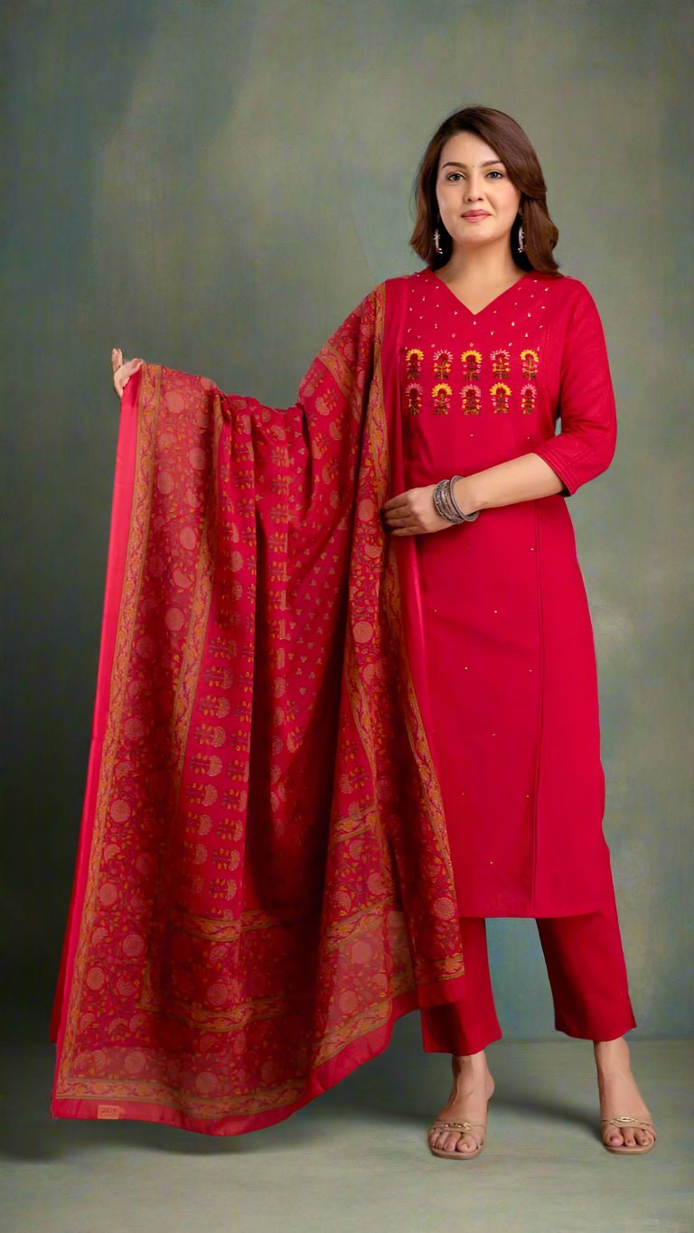Woman in a red traditional kurta set with a patterned dupatta against a textured wall.